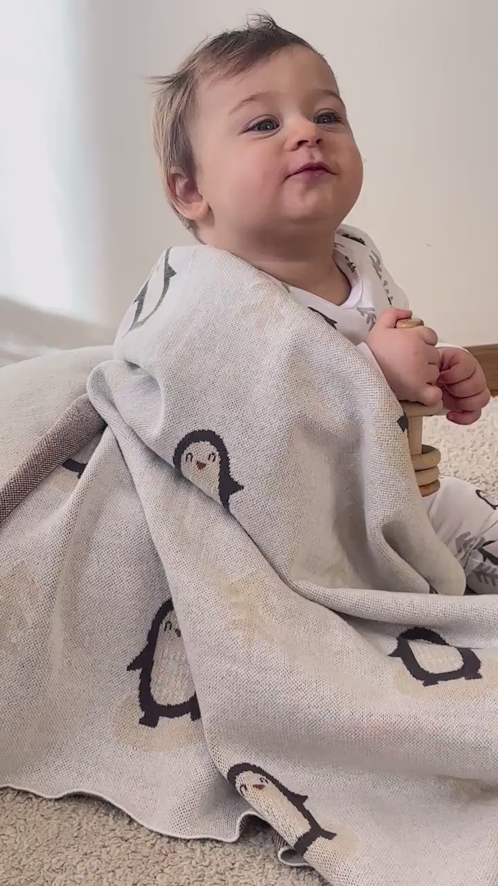 Baby wrapped in Arctic Penguins blanket sitting on the floor