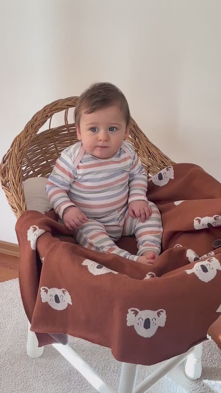 Baby wrapped in Happy Koala knit blanket while sitting in a chair