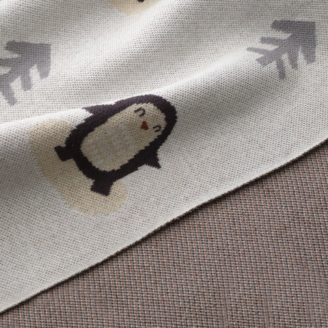 Close-up of penguin and tree design on organic cotton knit baby blanket