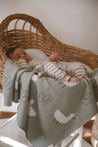 Baby lying in a woven basket wrapped in Minty Duck baby blanket