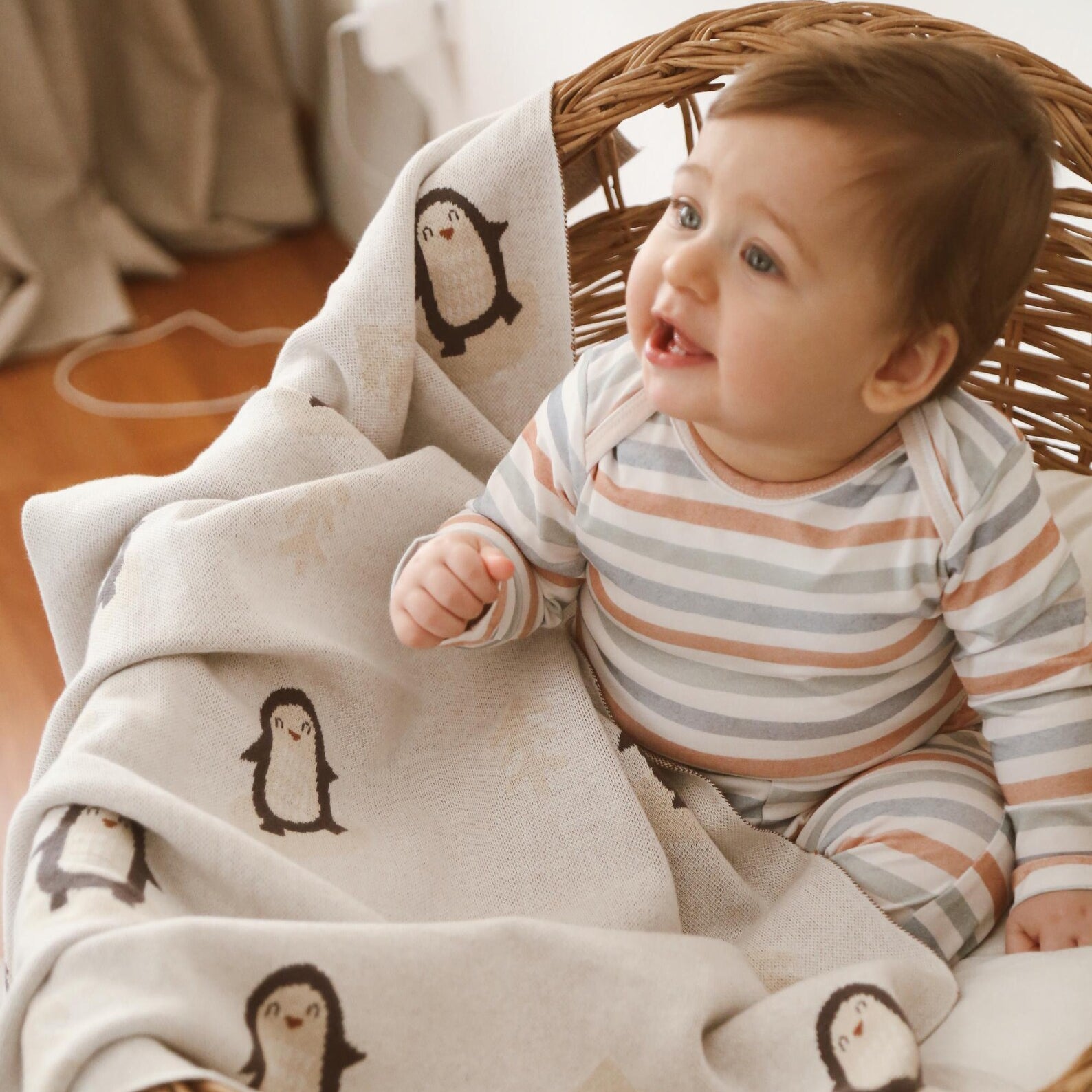 Smiling baby sitting in basket wrapped in Arctic Penguins baby blanket