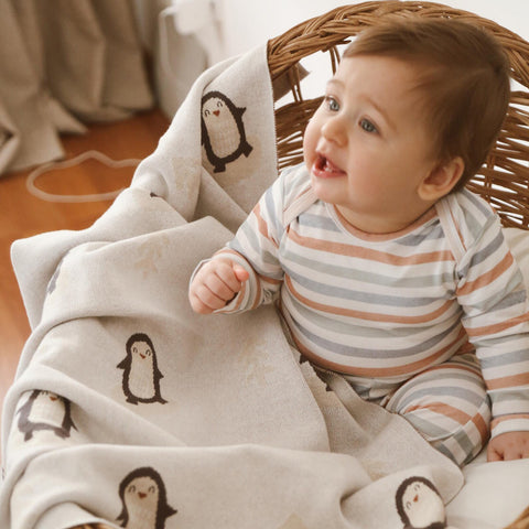 Smiling baby sitting in basket wrapped in Arctic Penguins baby blanket