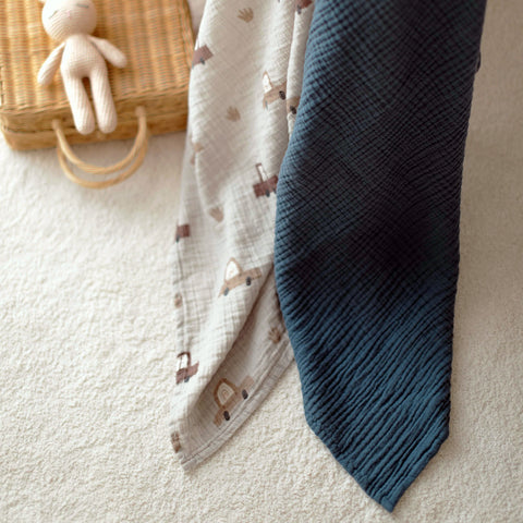 Cars swaddle and navy muslin blanket draped over crib side