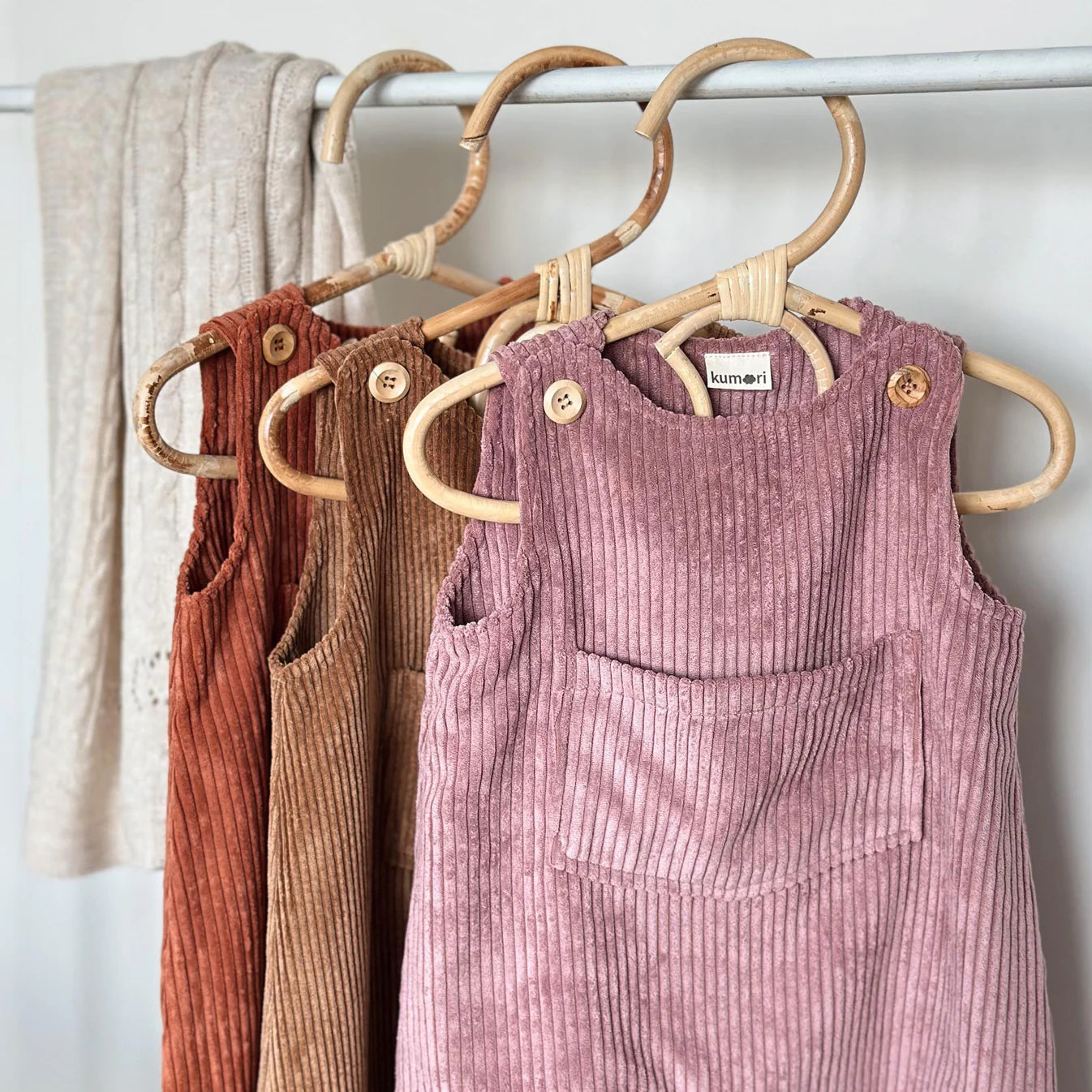 Assorted corduroy baby overalls including dusty pink hanging on a rack