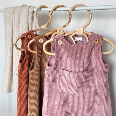 Assorted corduroy baby overalls including dusty pink hanging on a rack