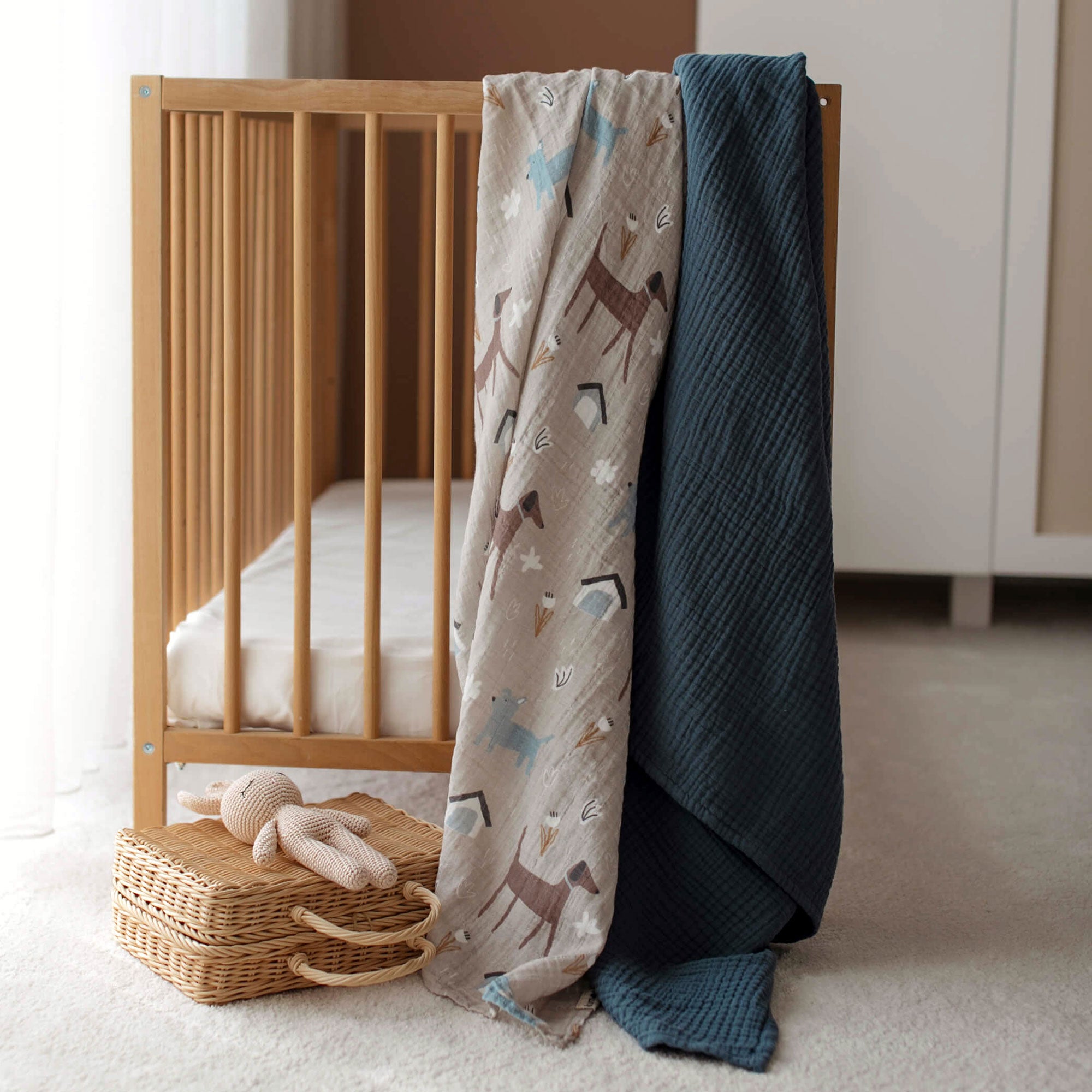 Dog swaddle and navy muslin blanket draped over crib rail