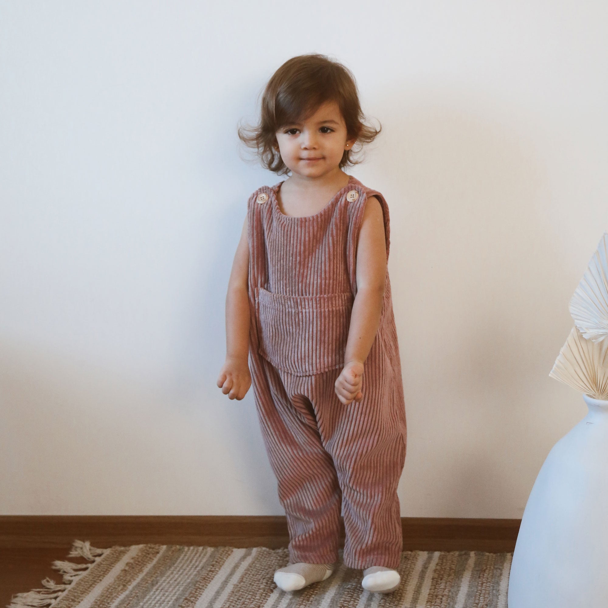 Toddler standing in dusty pink corduroy overalls with oversized front pocket