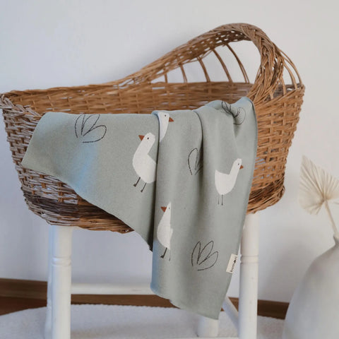Minty Duck baby blanket draped on chair basket showing full knit design