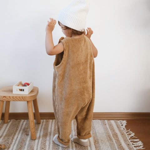 Back view of toddler wearing mustard baby corduroy overalls and white beanie