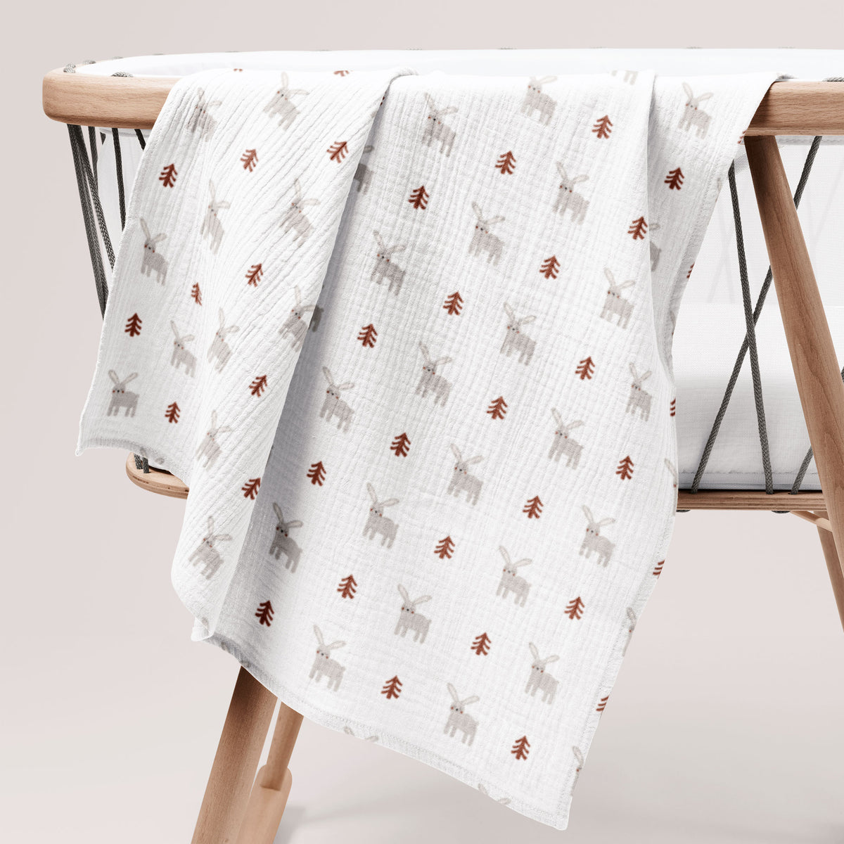 White cotton muslin swaddle with bunny print hanging on a wooden chair