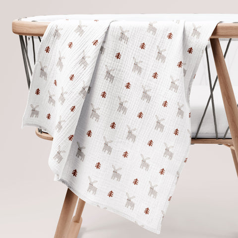 White cotton muslin swaddle with bunny print hanging on a wooden chair