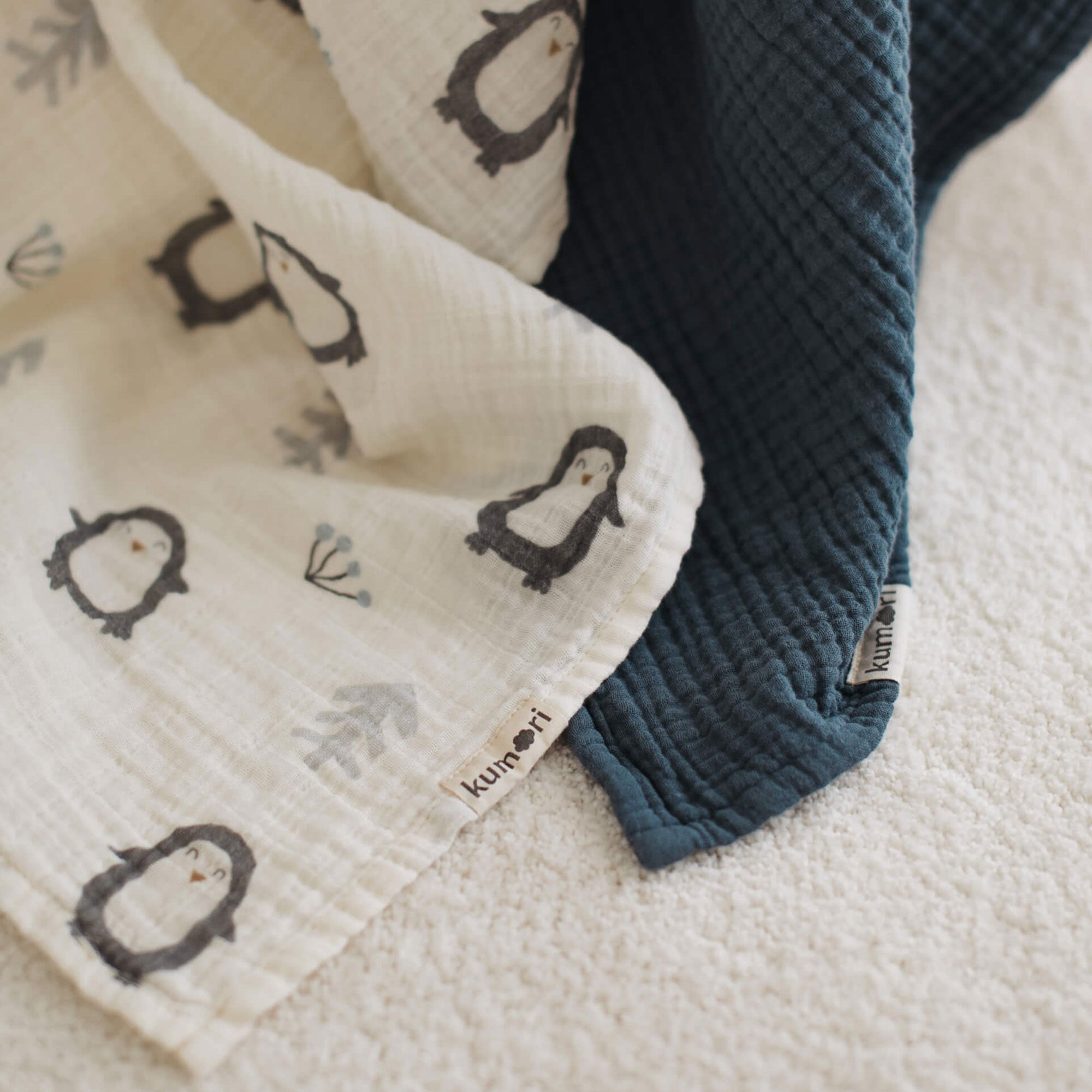 Close-up of penguin print muslin swaddle and textured navy blanket