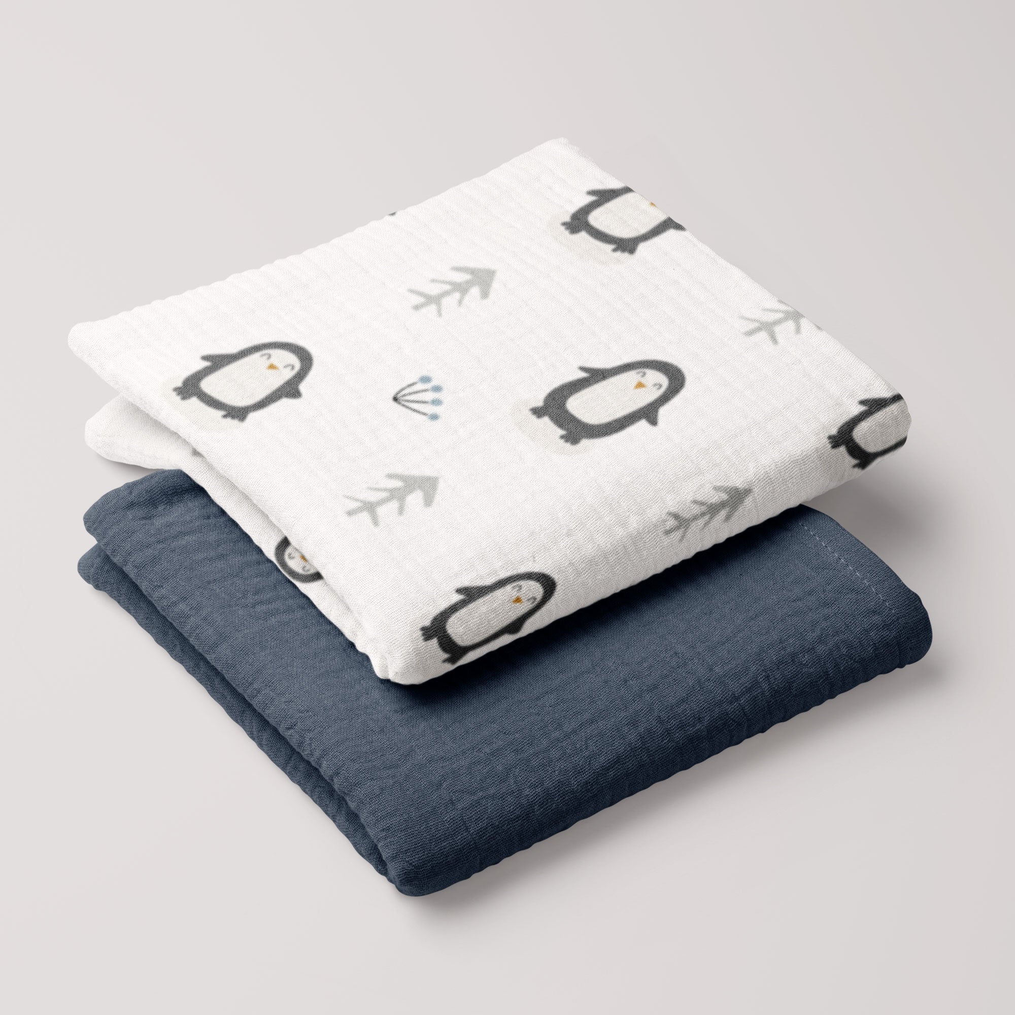 Penguin muslin swaddle and navy 4-ply blanket folded in a neat stack