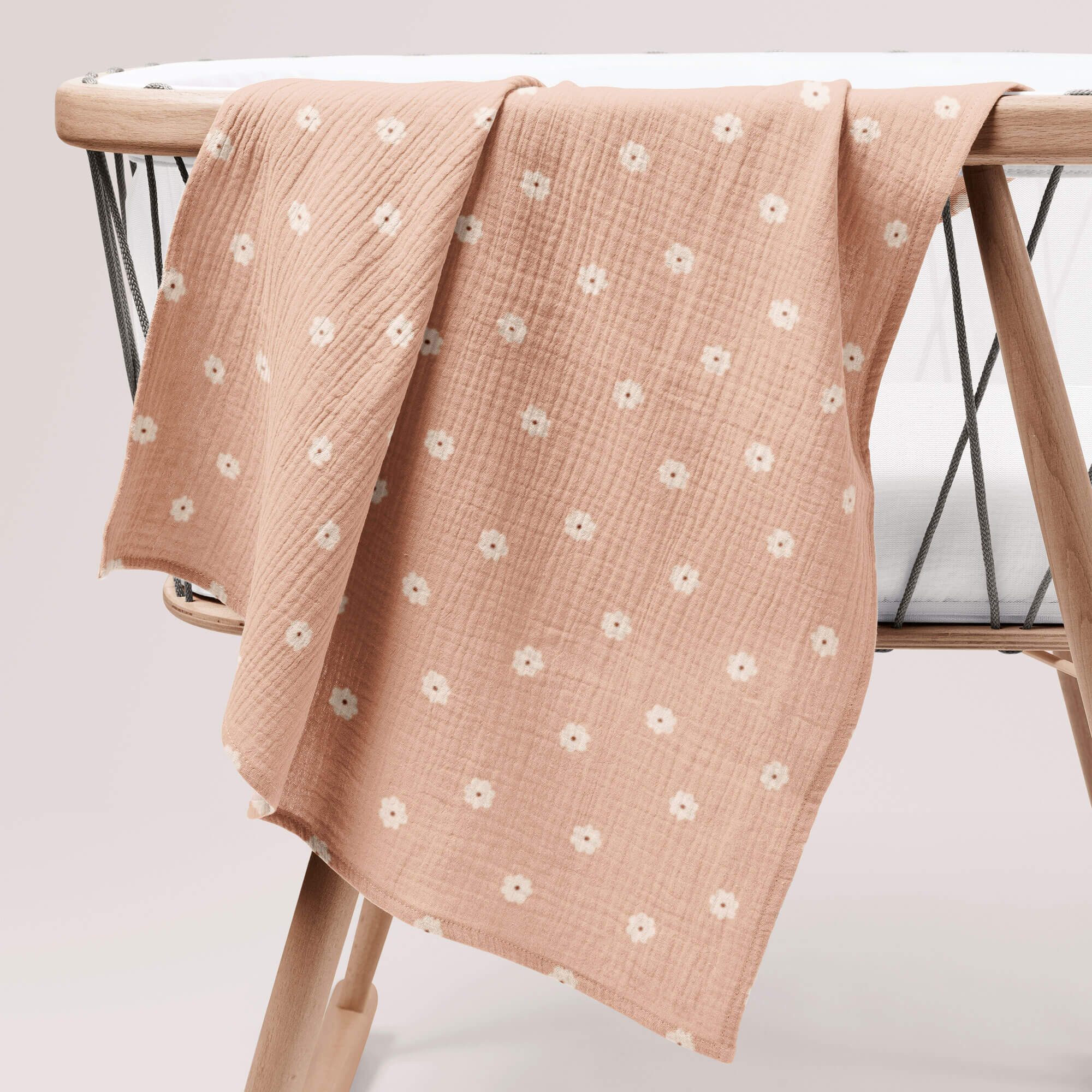 Salmon pink muslin swaddle with white poppy print draped over wooden crib