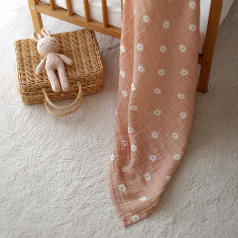 Salmon poppy swaddle with soft toy on white rug next to wicker basket
