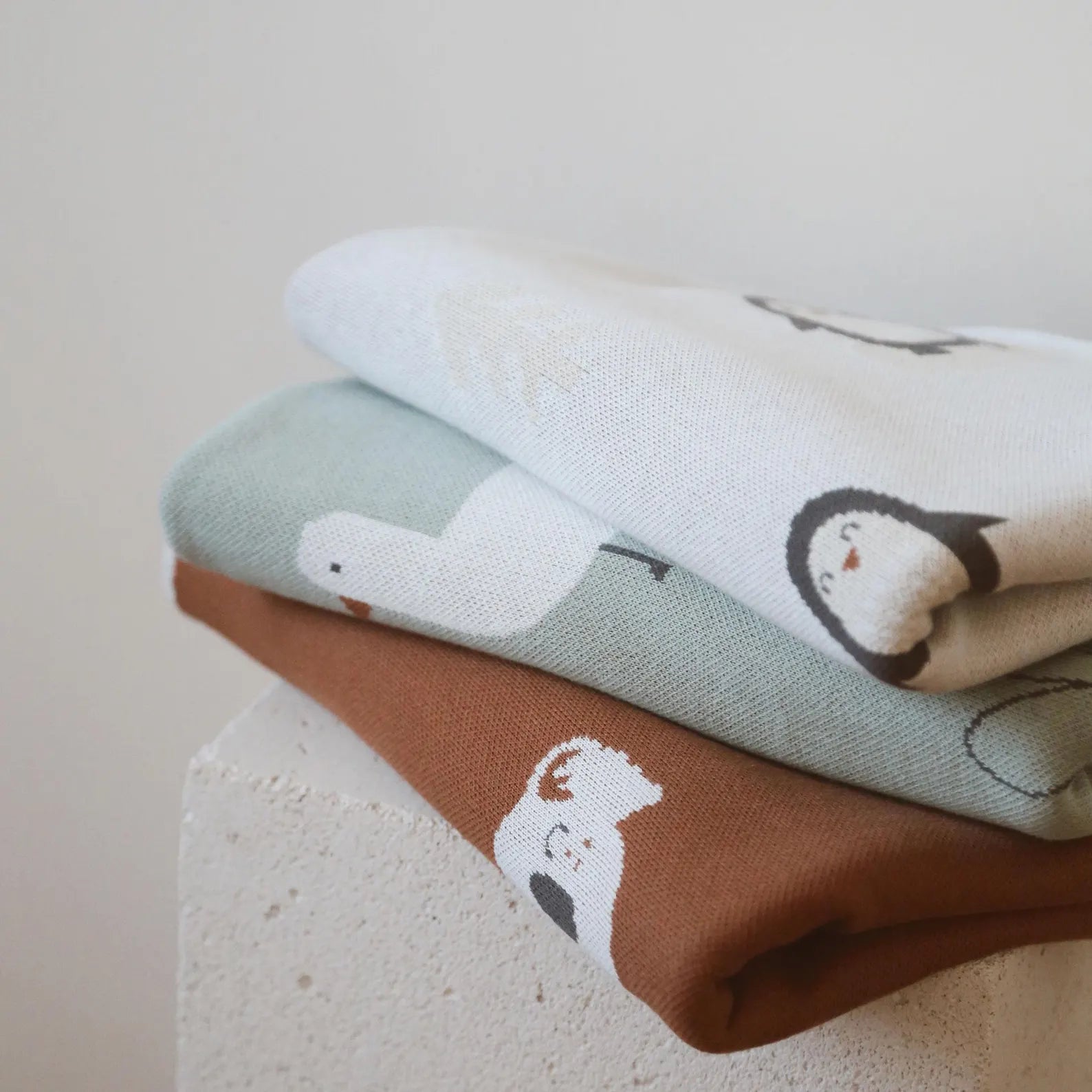 Stack of organic knit baby blankets featuring duck, penguin, and koala patterns