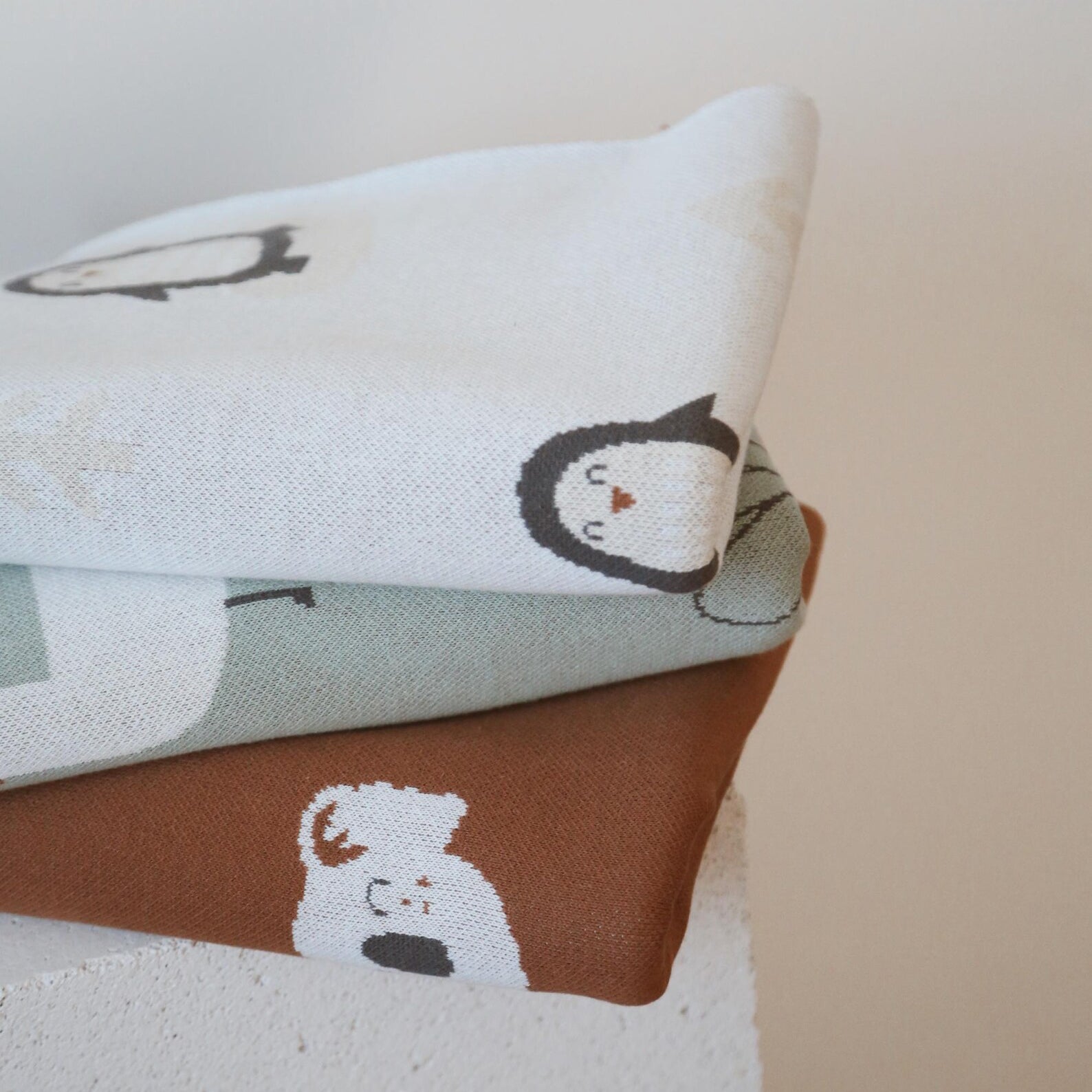 Stack of knit baby blankets including Arctic Penguins and Happy Koala designs