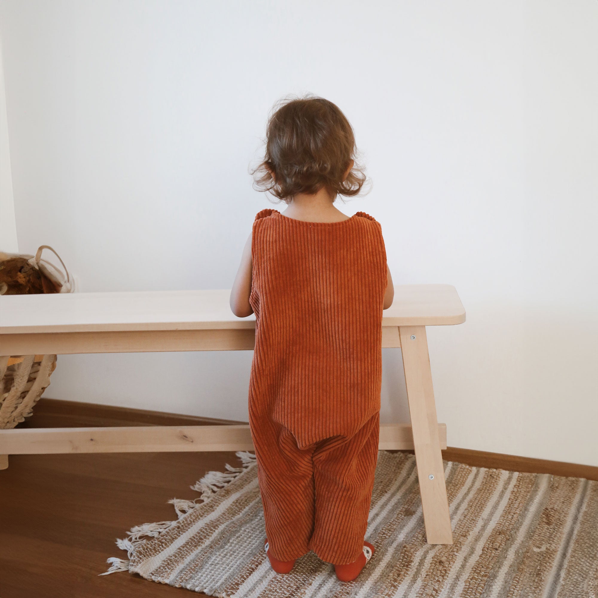 Back view of toddler wearing terracotta baby corduroy overalls at table