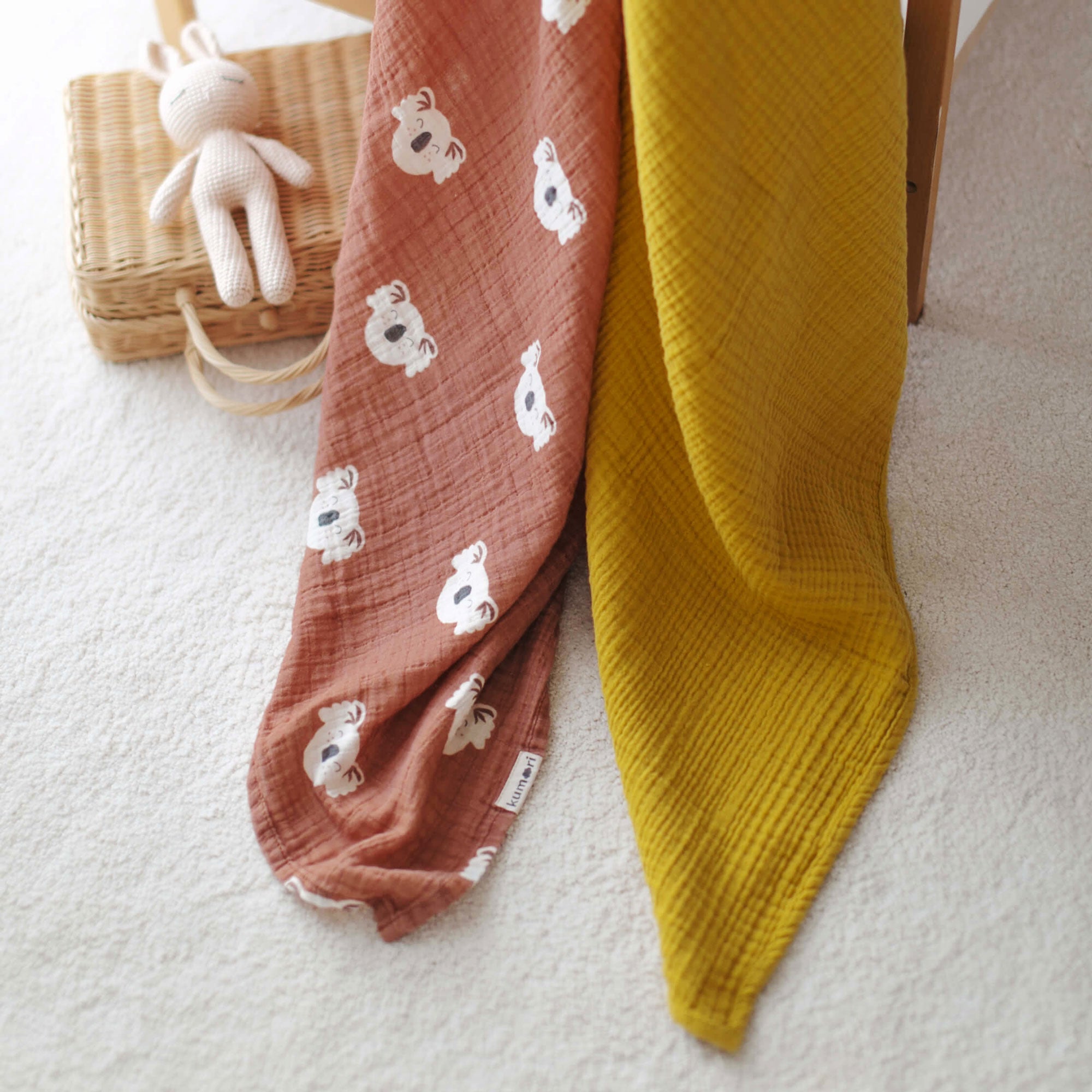 Koala swaddle and mustard muslin blanket styled in nursery setting by crib