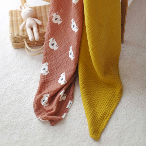 Koala swaddle and mustard muslin blanket styled in nursery setting by crib