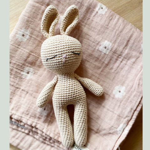 Cream sleep bunny laying on floral muslin swaddle