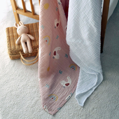Lady Goose muslin swaddle and white blanket draped over crib rail