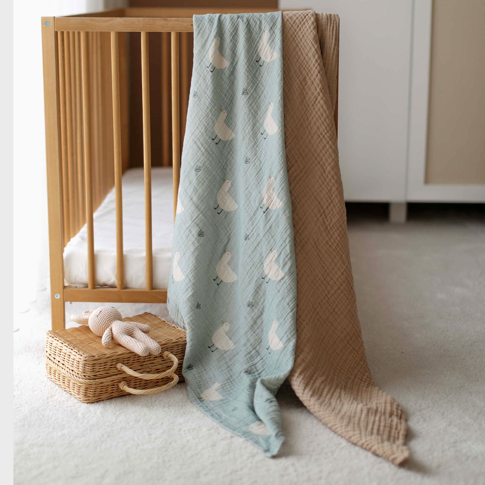 Minty Duck swaddle and latte muslin blanket hanging over a crib rail