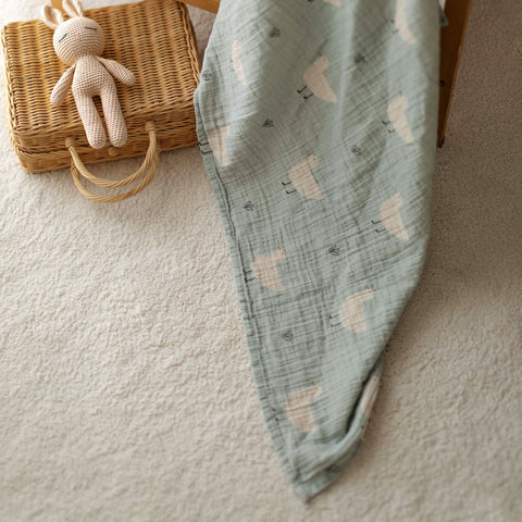 Close-up of Minty Duck muslin swaddle draped near wooden crib