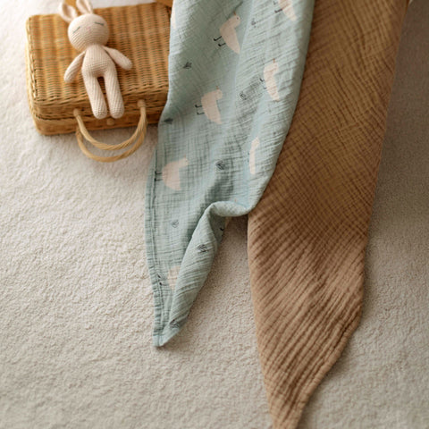 Draped Minty Duck swaddle next to latte muslin blanket