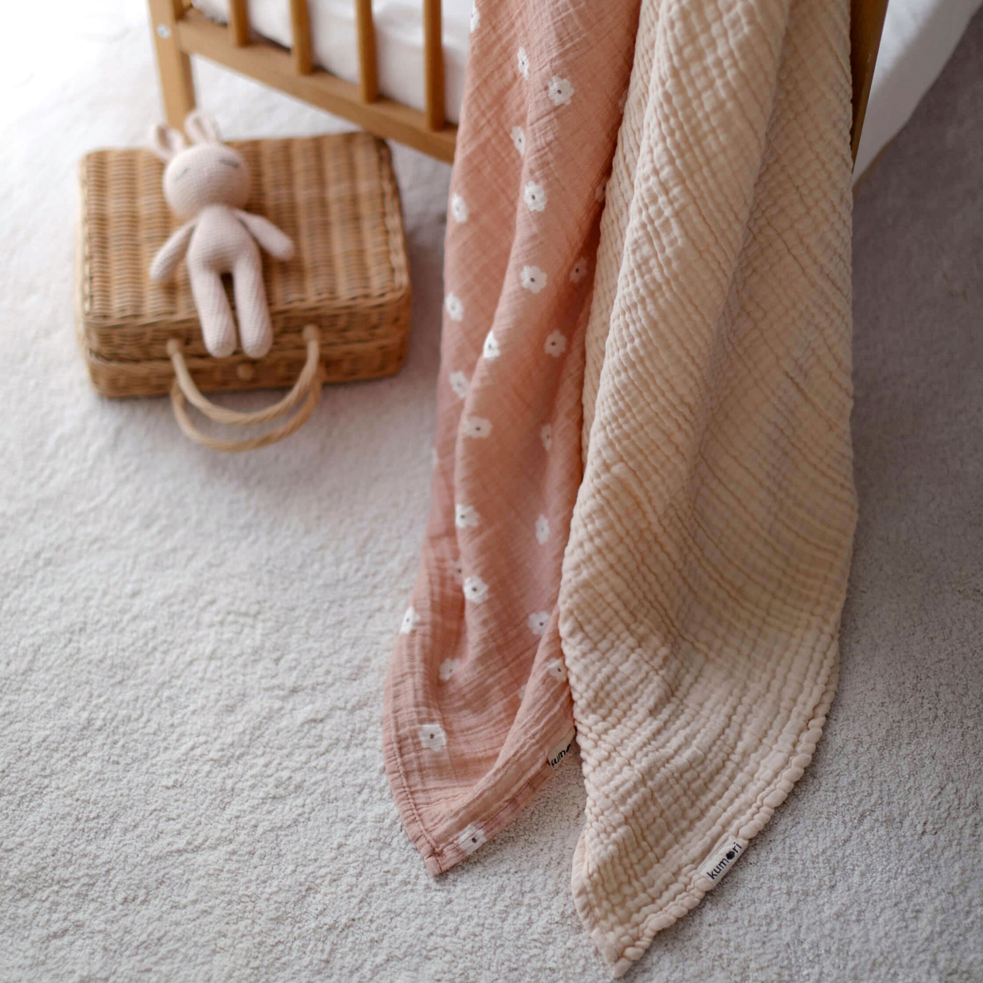 Salmon Poppy and cream muslin blankets draped beside wicker basket and soft toy