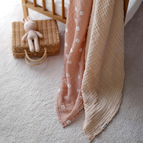 Salmon Poppy and cream muslin blankets draped beside wicker basket and soft toy