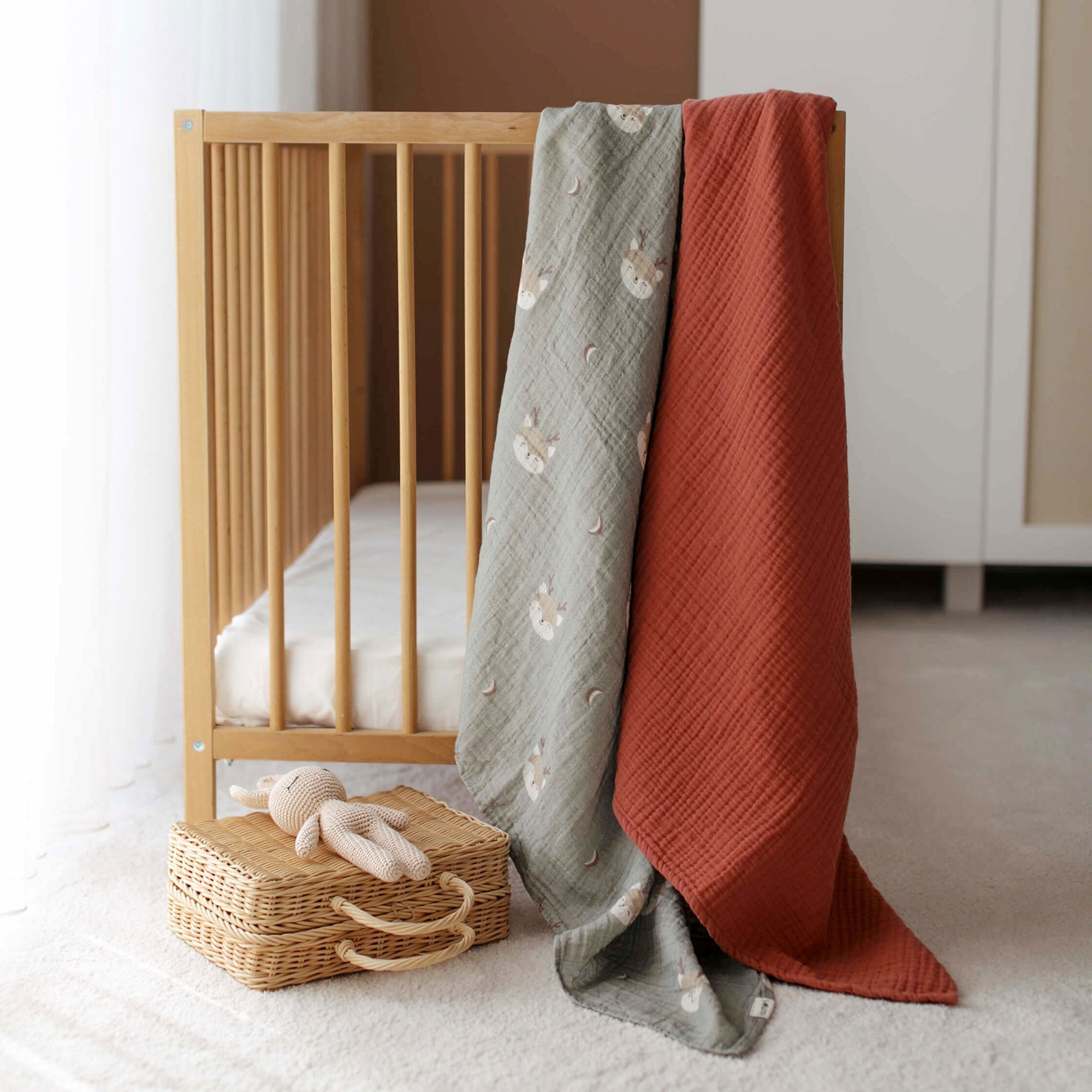 Terra cotta blanket and Forest Deer swaddle draped over crib rail